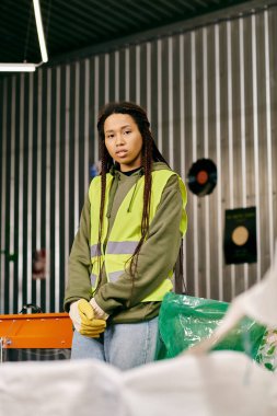 A young volunteer in a yellow vest sorts waste in a warehouse, embodying eco-conscious practices. clipart