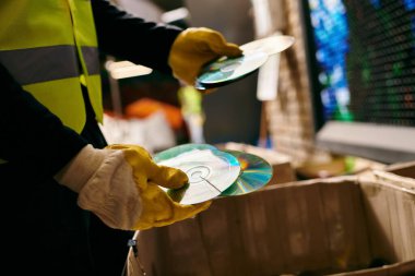 A young volunteer in a yellow safety vest sorts waste, holding cd with eco-conscious intentions.
