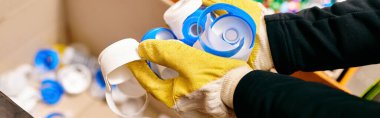 A young volunteer clad in a safety vest carefully sorts waste while wearing a pair of vibrant yellow gloves.
