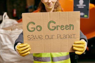 A young volunteer in gloves and safety vest holds a sign that says go green save our planet in a passionate call to action. clipart