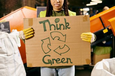 A young volunteer in gloves and safety vest holds a sign saying think green, promoting environmental awareness through action.