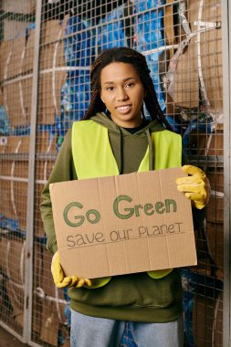 A woman in gloves and safety vest holds a sign urging to go green and save our planet.