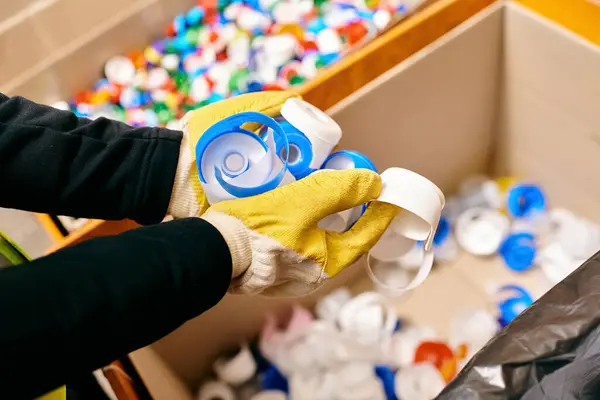 stock image A person in a yellow glove holds a bottle while sorting waste, embodying eco-conscious practices.