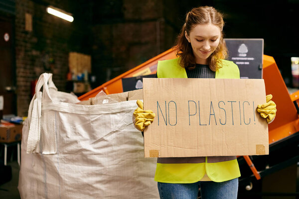 A young volunteer in gloves and safety vest holding a sign that reads no plastic at a waste sorting event.