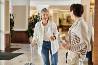 Senior lesbian couple walks with her luggage. clipart