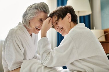 Two senior women share a moment of laughter on a cozy bed. clipart