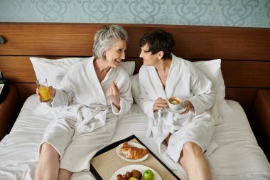 Huzur dolu bir anı paylaşan, rahat bir yatakta oturan son sınıf lezbiyen bir çift..