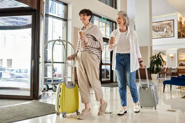 Senior lesbian couple with luggage, standing affectionately.