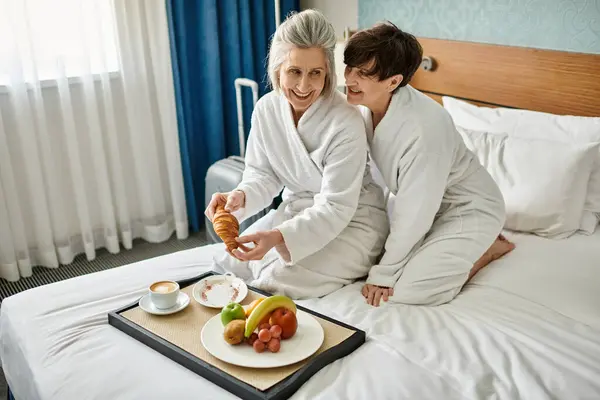 シニアレズビアンカップルは ホテルの部屋で居心地の良いベッドに座って柔らかい瞬間を楽しんでいます — ストック写真