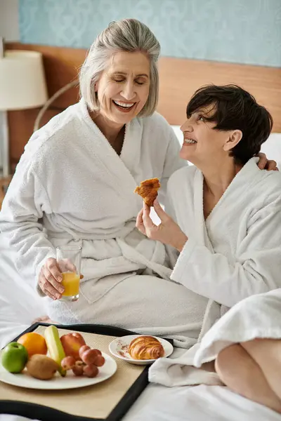 stock image Two senior lesbian women lovingly embrace while sitting on a bed in a hotel room.