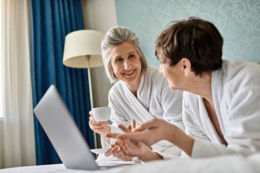 A senior lesbian couple sharing a conversation in a cozy hotel room. clipart