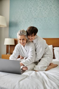 Senior lesbian couple engrossed in laptop on bed. clipart