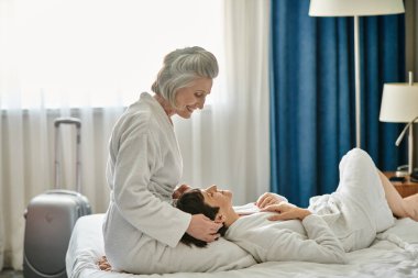 A senior lesbian couple tenderly embracing while laying on a bed. clipart