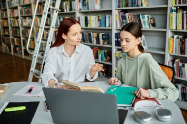 A redhead tutor providing after-school lessons to a teenage girl in a library, using a laptop for modern education. clipart