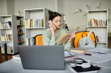 Teenage girl multitasks with laptop open, talking on phone in library setting after school. clipart