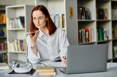 Kızıl saçlı bir bayan öğretmen, okuldan sonra bir dizüstü bilgisayar kullanarak online bir ders vermeye odaklanmış..