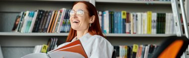 A red-haired woman immersed in a book in a library, engrossed in learning and exploration. clipart