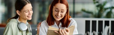 Bir öğretmen, kızıl saçlı bir kadın, her ikisi de modern bir öğrenim ortamının ortasındaki bir kitaba dalmış genç öğrencisine bilgi veriyor..