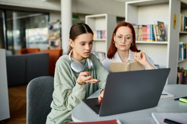 A redhead woman teaches a teenage girl at a table, both focused on a laptop during an after-school lesson. clipart