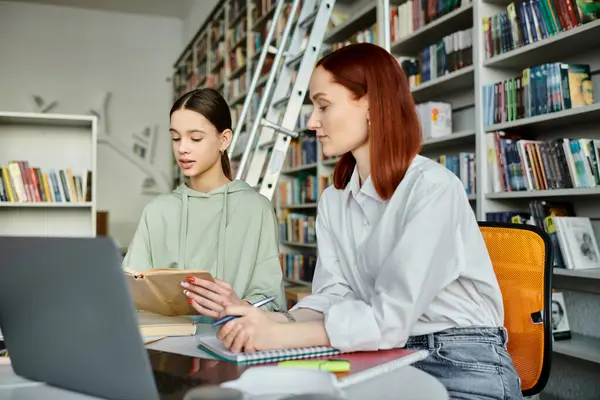 Kızıl saçlı bir öğretmen ve genç bir kız kütüphane masasında hayat dolu dersler alıyor, dizüstü bilgisayara odaklanmış..