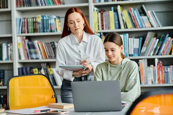 stock image Redhead tutor teaches teenage girl, both focused on a laptop in a library. Modern education and after-school lessons.