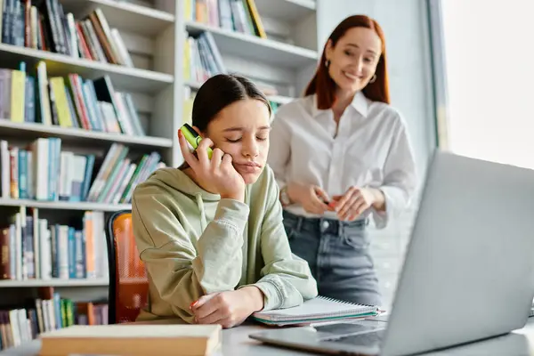 stock image A focused redhead tutor multitasks, teaching a teenage girl while talking on the phone and using a laptop for after-school lessons.