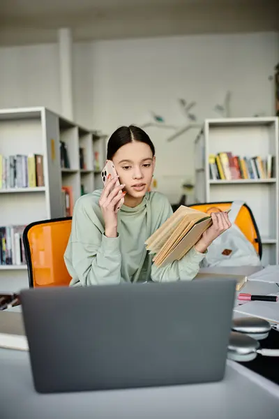 stock image A young woman immersed in her studies, sitting at a desk with a laptop and a book, focusing on modern education.