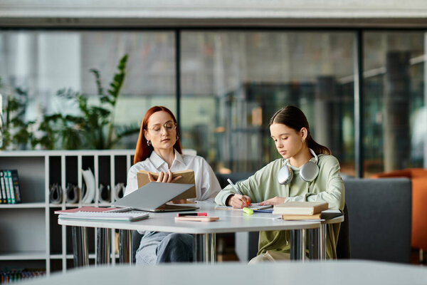 Рыжая женщина репетирует с девочкой-подростком в библиотеке, обе занимаются внешкольными уроками на ноутбуке.