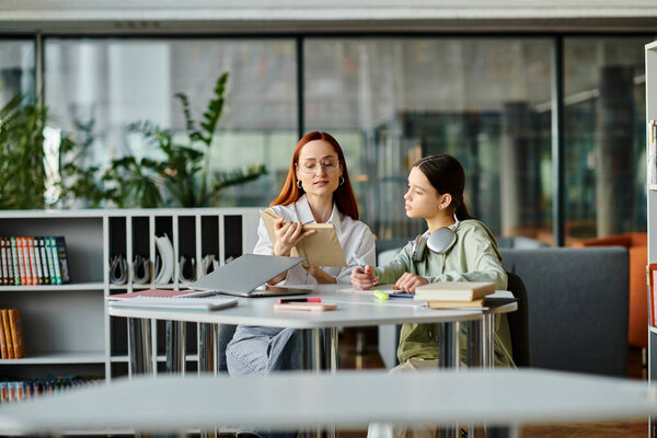 A redhead woman tutors a teenage girl in a library, both engrossed in learning while using a laptop for modern education.