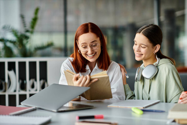 A redhead woman mentors a teenage girl at a table, immersed in a book during after-school lessons.