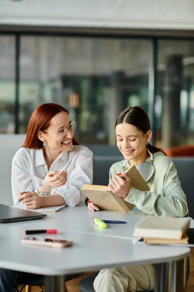 stock image A redhead woman tutors a teenage girl at a table with a laptop, engaging in after-school lessons.