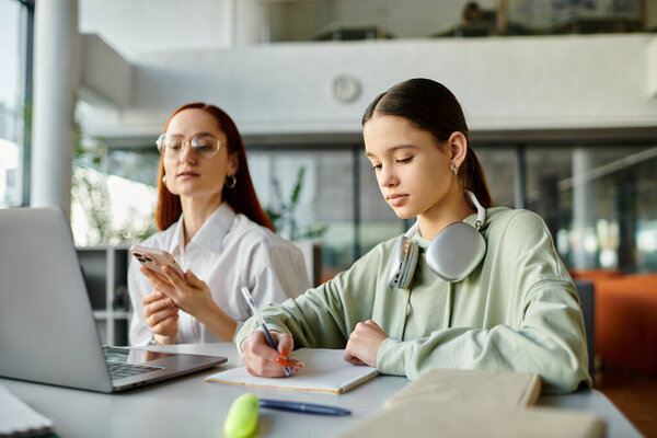 Девушка-подросток с рыжими волосами сидит за столом в наушниках и пользуется ноутбуком во время занятий после школы со своим репетитором.