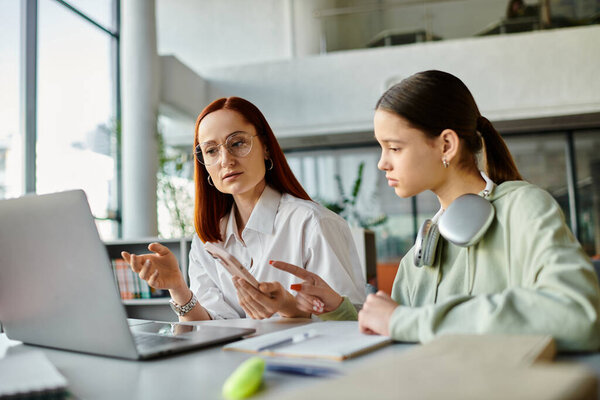 Рыжая женщина учит девочку-подростка, репетиторство после школы вместе с помощью ноутбука.