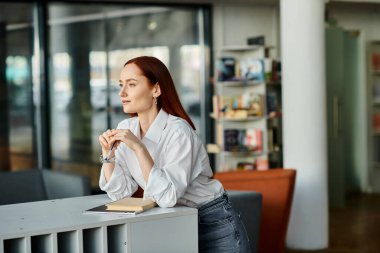 A redhead woman sitting at desk in a library, modern education. clipart