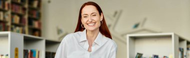 A redheaded woman smiles after tutoring in a library, after-school lessons. clipart