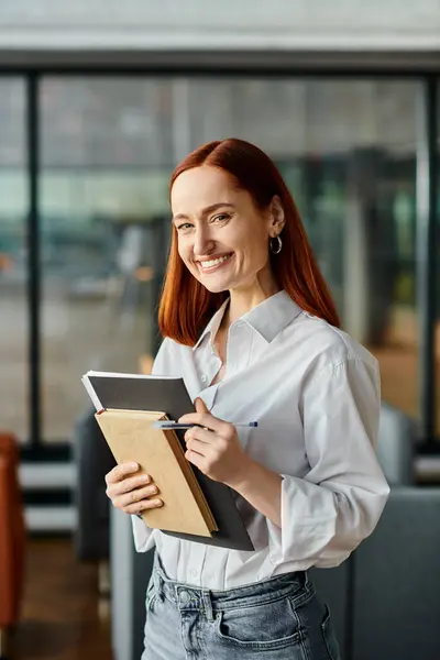 stock image A redhead woman holding a notebook and book for after-school lessons.