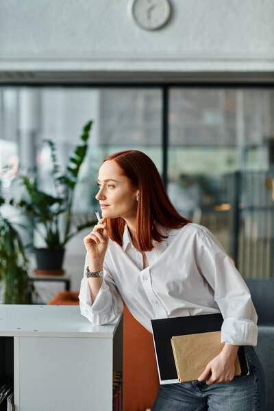 Рыжий репетитор в белой рубашке прислоняется к столу, после уроков.