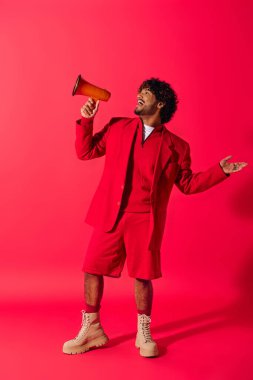 Canlı kırmızı takım elbiseli genç Hintli adam canlı bir arkaplana karşı kırmızı bir megafon tutuyor..