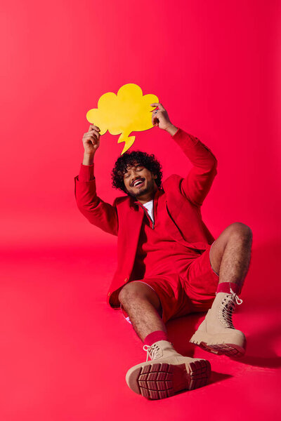 Человек в ярком костюме сидит на земле, держа речевой пузырь..