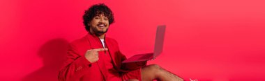 Kırmızı ceketli genç Hintli adam dizüstü bilgisayar tutuyor..