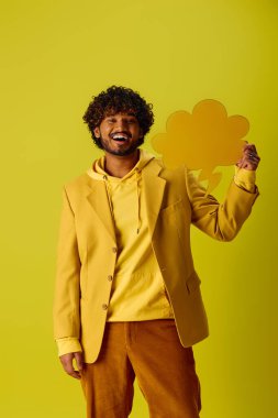 Handsome young Indian man in vibrant yellow jacket and brown pants posing against vivid backdrop. clipart