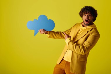 Young Indian man stylishly holds a speech bubble in a vibrant yellow jacket against a colorful backdrop. clipart