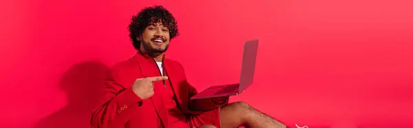 stock image Young Indian man in red jacket holds laptop.