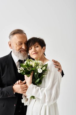 Gelinlik giymiş orta yaşlı bir gelin ve damat özel günlerini stüdyo ortamında yan yana durarak kutluyorlar..