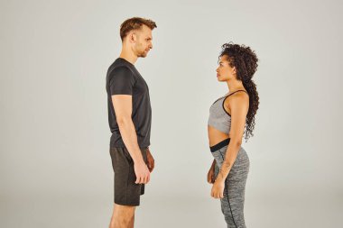 Aktif giyinen genç bir ırklar arası spor çifti gri bir arka plana karşı stüdyoda yan yana dururlar..