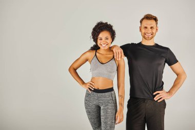 Spor kıyafetleri içinde genç bir erkek ve kadın gri bir stüdyo arkaplanına karşı şık bir poz veriyorlar..