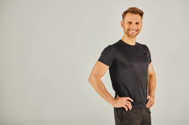 Genç bir sporcu stüdyo ortamında siyah tişört giyerken kendine güvenen bir poz verir..