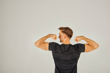 Genç bir atletik adam beyaz bir arka plan önünde kaslarını esnetir, güç ve kararlılık gösterir..
