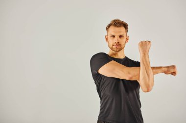 Aktif giyinmiş genç bir atletik kollarını gri bir arka plana yaslayarak dinamik bir güç ve zindelik gösterisi yapıyor..