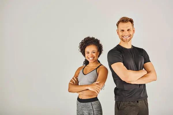 stock image A young interracial sport couple, wearing active wear, striking a pose together in a studio against a grey background.